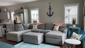 A modern living room with a grey sectional sofa, a small round table, and a blue chair. - Sebago Lake, Maple Cove, Lake House (Casco)