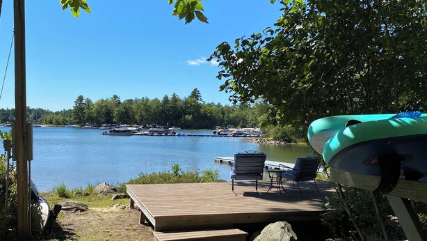 A lakeside deck with a view of the lake, a dock, and boats. - Sebago Lake, Maple Cove, Lake House (Casco)