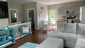 A modern living room with a grey sofa, a blue chair, and a kitchen area with grey cabinets and a microwave. - Sebago Lake, Maple Cove, Lake House (Casco)
