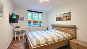 Ein Schlafzimmer mit einem Bett, einem Schreibtisch, einem Stuhl, einem Fenster und einem Bild an der Wand.