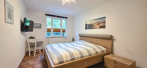 A bedroom with a bed, a desk, a chair, a window, and a picture on the wall.