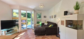 A living room with a flat-screen TV, a sofa, a glass coffee table, and a potted plant. - FEWO i35 - 3-room apartment close to the beach for 4 people with WLAN (Graal-Müritz)