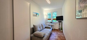 A narrow hallway with a sofa, a radiator, a television, and a window with blinds. - FEWO i35 - 3-room apartment close to the beach for 4 people with WLAN (Graal-Müritz)
