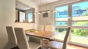 Ein Essbereich mit einem Holztisch, zwei Stühlen, einem Fenster mit Jalousien und einem Küchenbereich mit Schränken.