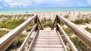 En träpromenad som leder till en strand med kristallklart turkost vatten och en molnig himmel.