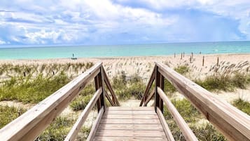 Une promenade en bois menant à une plage aux eaux turquoise et limpides, sous un ciel nuageux.