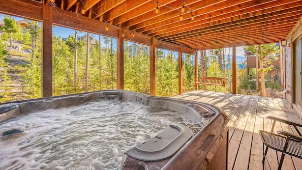 Een hottub op een houten terras met uitzicht op bomen en een gebouw op de achtergrond.