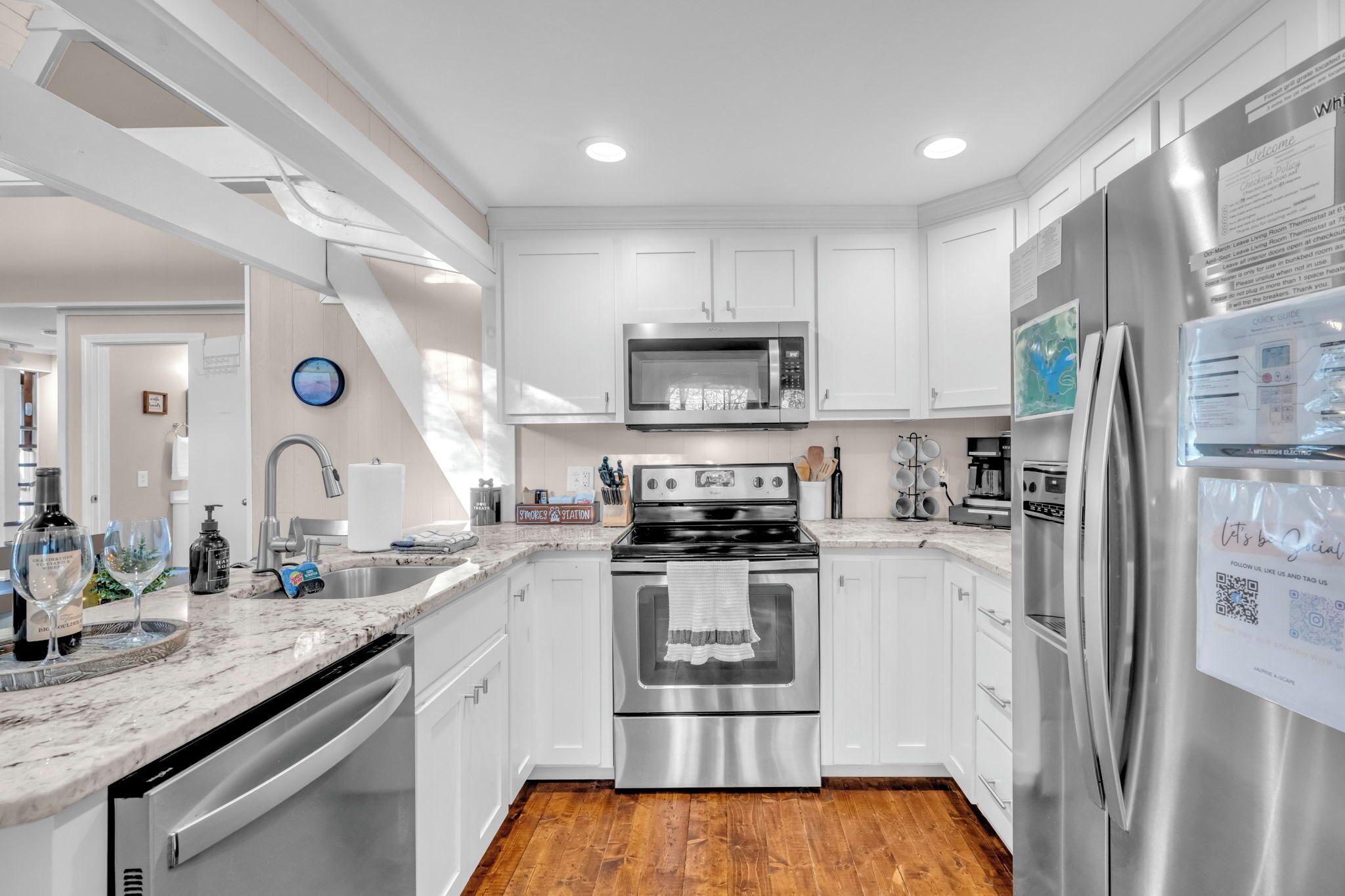 A modern kitchen with white cabinets, stainless steel appliances, and a wooden floor.