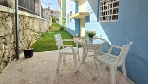 A patio with a round table and four chairs, a potted plant, and a view of a building with a blue facade.