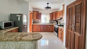 A kitchen with wooden cabinets, a granite countertop, a refrigerator, a microwave, and a stove.