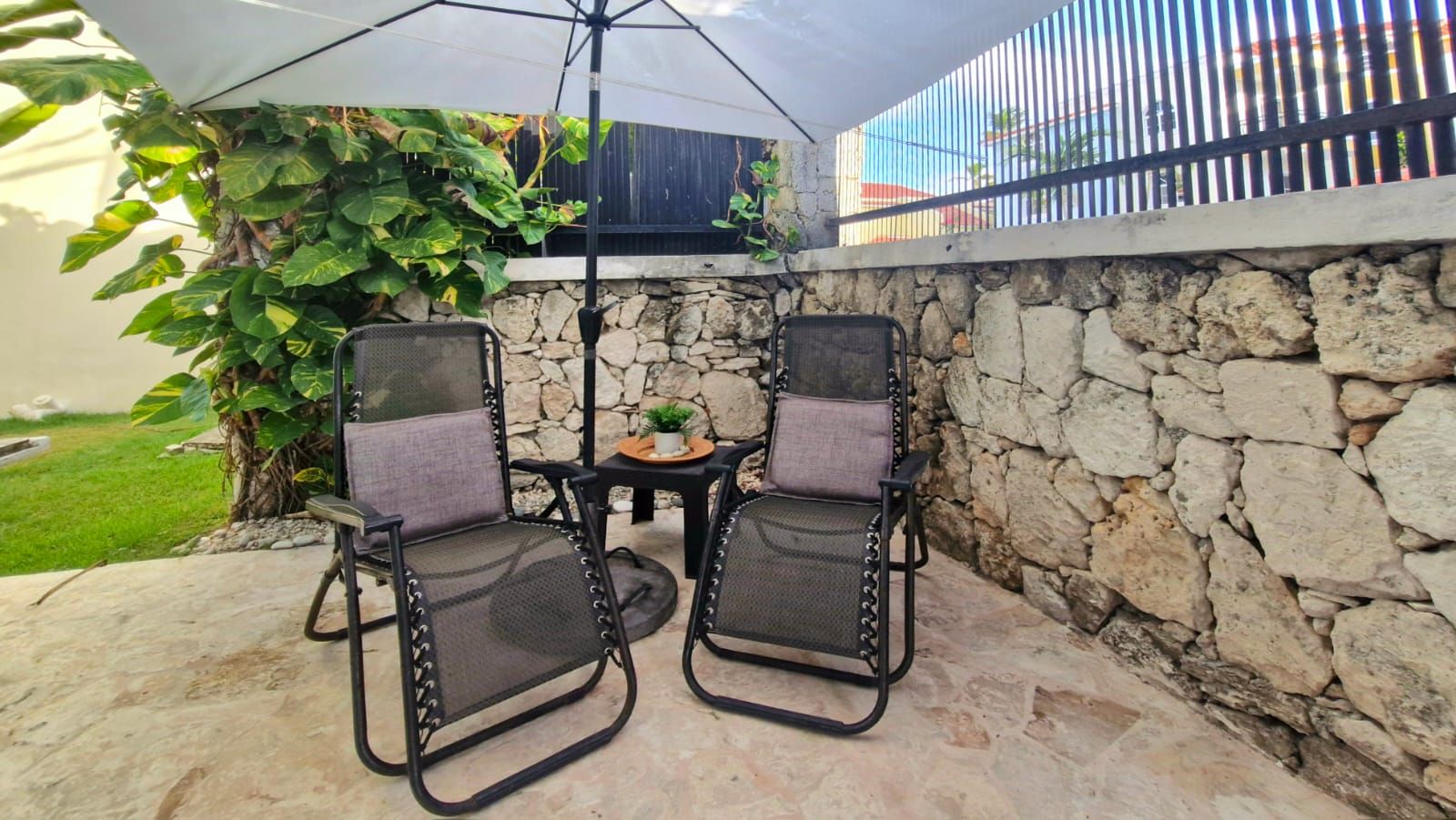 Une terrasse extérieure avec deux chaises et une table, entourée d’un mur de pierre et d’une zone abritée.