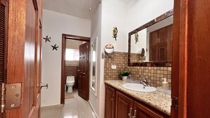 A bathroom with a wooden vanity, a sink, a mirror, and a toilet. - Lovely Spacious Condo with Pool View, Close to Beaches and Shops! (Punta Cana)