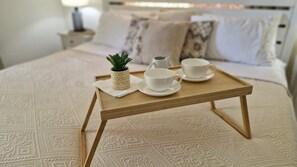 A bed with a patterned bedspread, a wooden tray with a pineapple, two white cups, and a small plant.