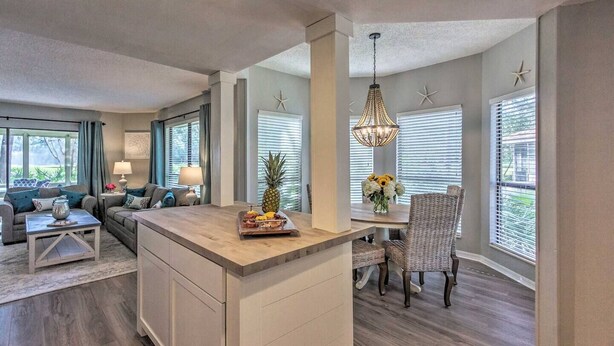 Een moderne keuken met een centraal eiland, een eethoek met rieten stoelen, en een woonkamer met een bank en salontafel.