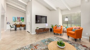 A spacious living room with a high ceiling, a flat-screen TV mounted on the wall, and a dining area with a table and chairs. - Beautiful 2 Bedroom 2 Bath Scottsdale Townhome (Scottsdale)