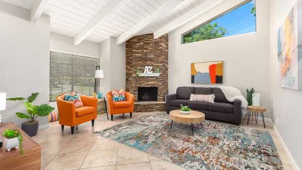 A spacious living room with a stone fireplace, two orange armchairs, a dark sofa, and a colorful rug. - Beautiful 2 Bedroom 2 Bath Scottsdale Townhome (Scottsdale)