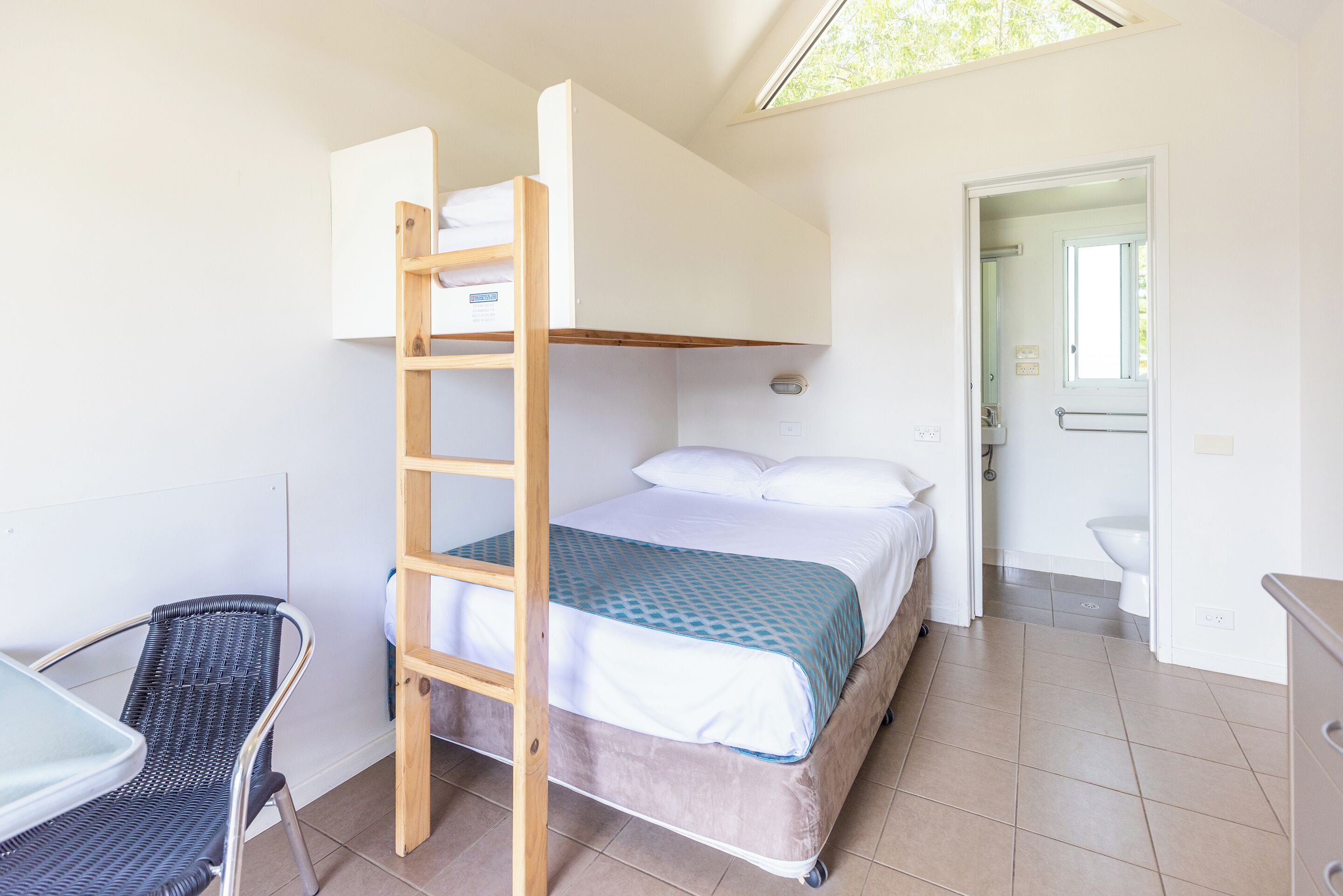 A compact room with a bunk bed, a desk with a chair, and a bathroom visible through an open door.