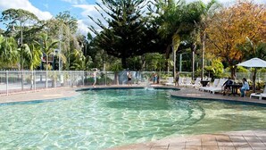 Una piscina con agua cristalina, rodeada por una valla blanca y varios árboles, incluyendo uno con hojas de colores otoñales.