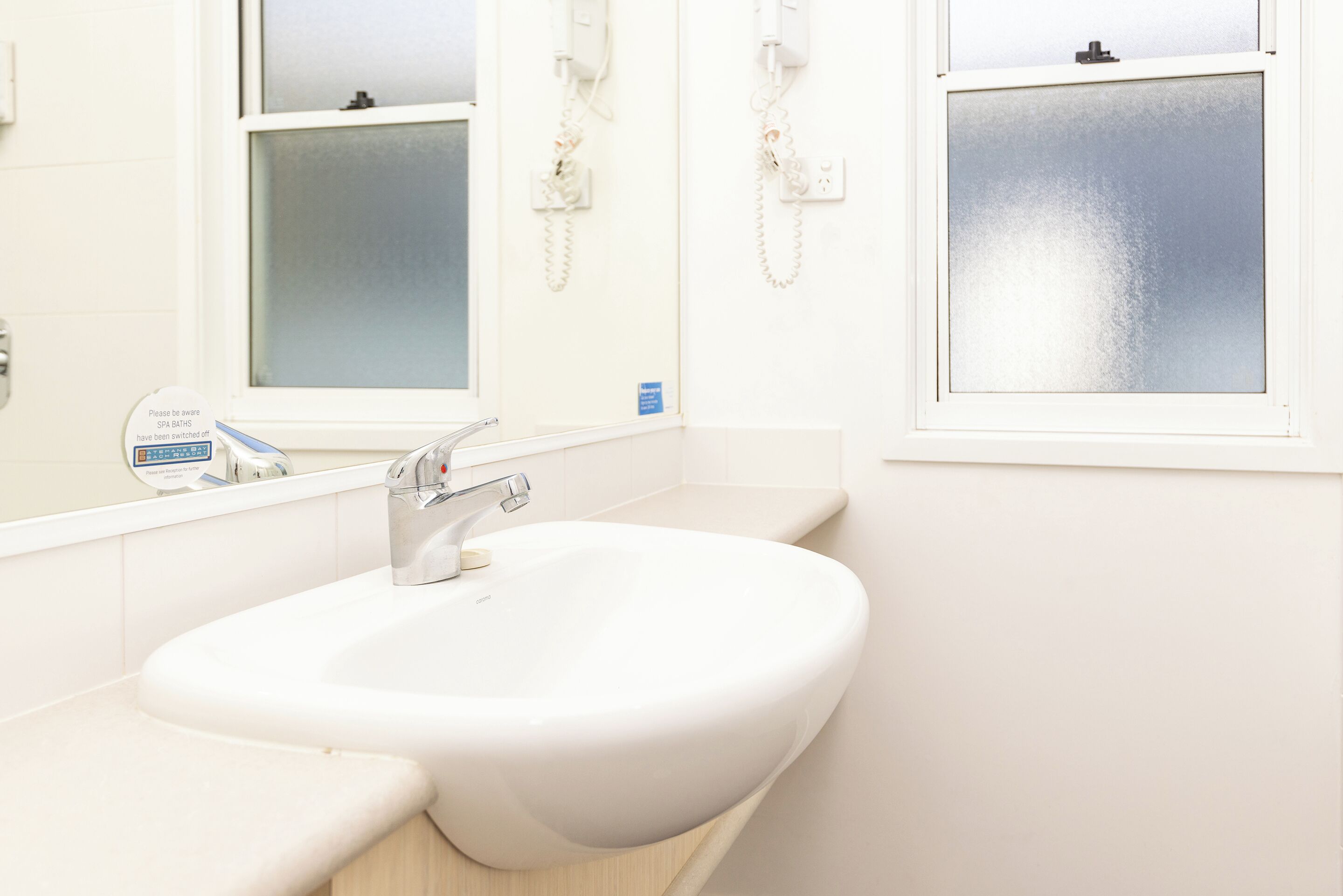A bathroom with a white sink, a mirror, and a window with frosted glass.
