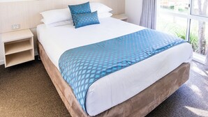 Una habitación de hotel con una cama, una mesita de noche, un ventilador de techo y una ventana con cortinas.