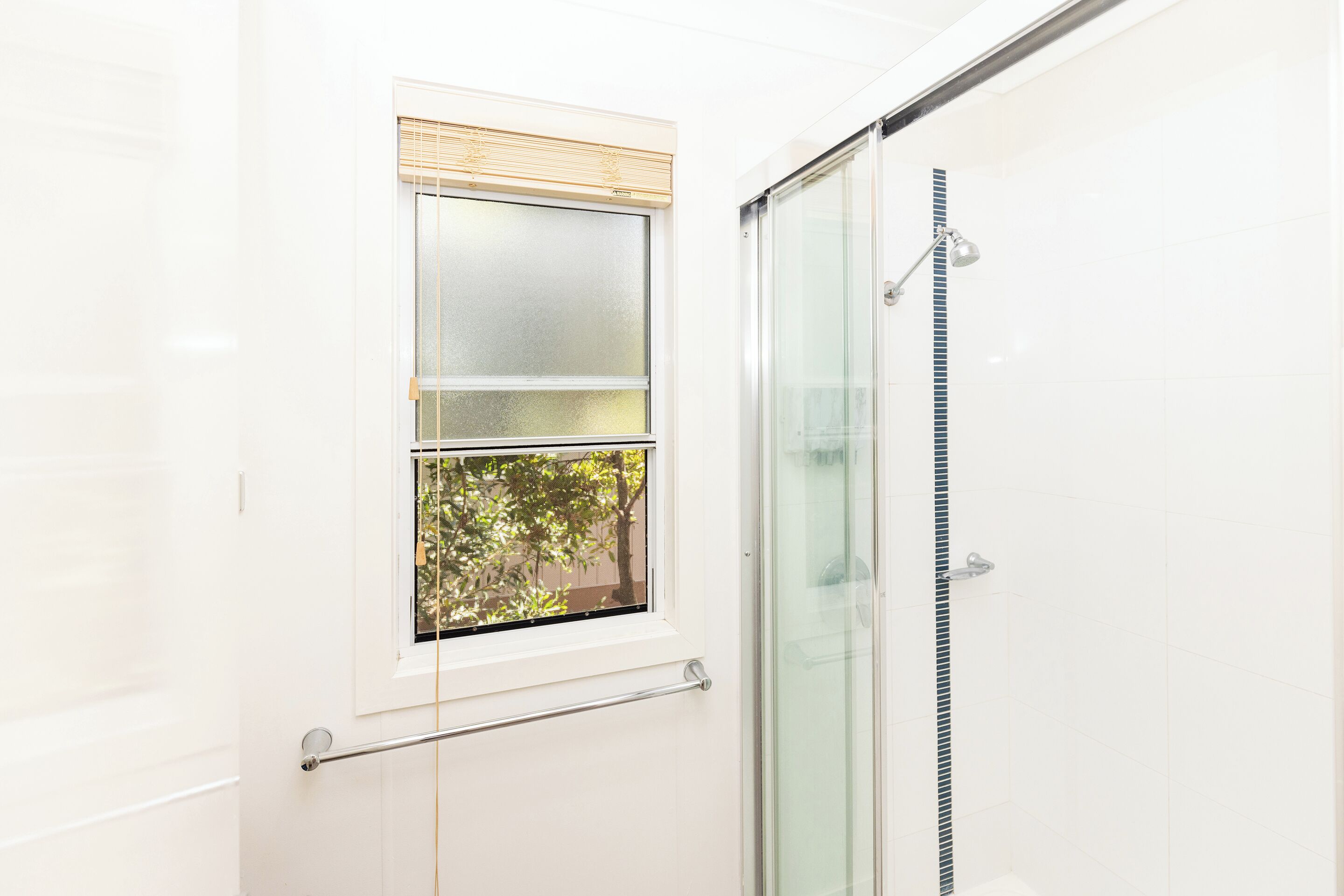 A bathroom with a glass shower enclosure, a window with blinds, and a towel rack.