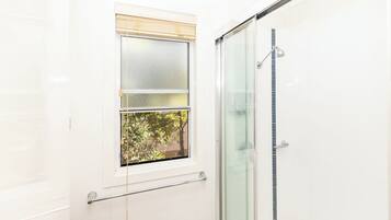 A bathroom with a glass shower enclosure, a window with blinds, and a towel rack.