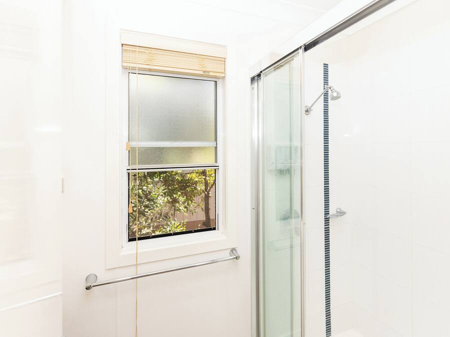 A bathroom with a glass shower enclosure, a window with blinds, and a towel rack.