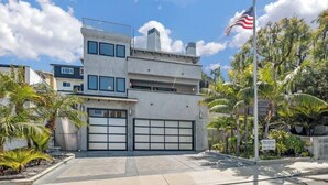 A modern multi-story building with a garage, surrounded by palm trees and an American flag. - Ocean view Surf Ghetto custom home (San Clemente)