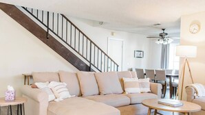 Ein Wohnzimmer mit einem beigefarbenen Ecksofa, einem Couchtisch und einer Treppe.