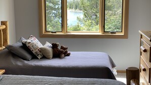 Ein Schlafzimmer mit zwei Betten, einem großen Fenster mit Blick auf einen See und Bäume sowie einer hölzernen Kommode.
