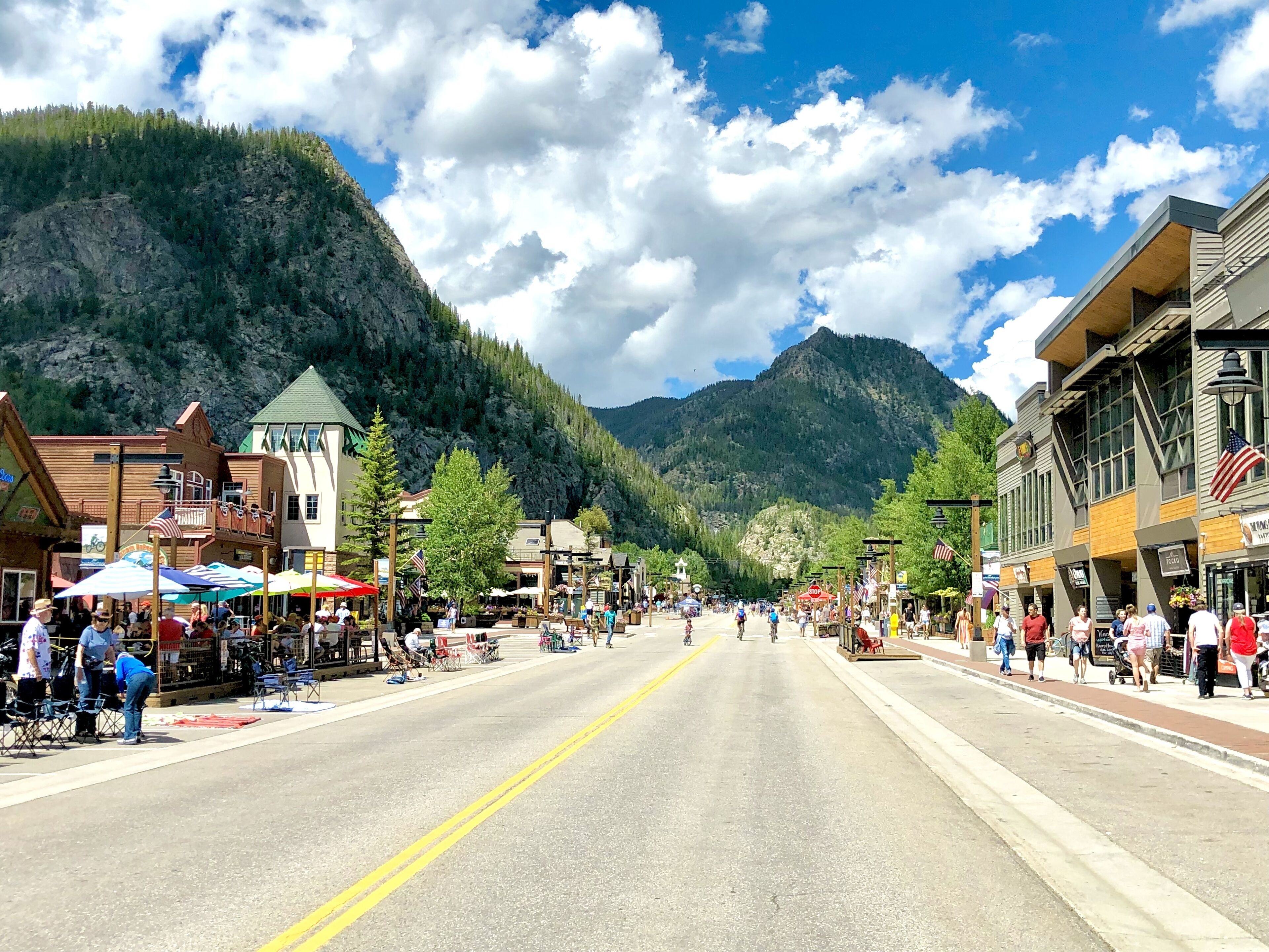 Eine Stadtstraße mit Gebäuden, Geschäften und einer Bergkulisse im Hintergrund.