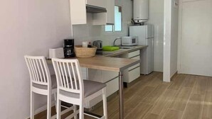 Una cocina compacta con armarios blancos, una encimera de madera y un lavamanos. Hay dos sillas blancas y una cafetera sobre la encimera.