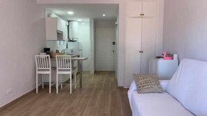 Una habitación con sofá blanco, una mesa de comedor con sillas, una zona de cocina y un armario.
