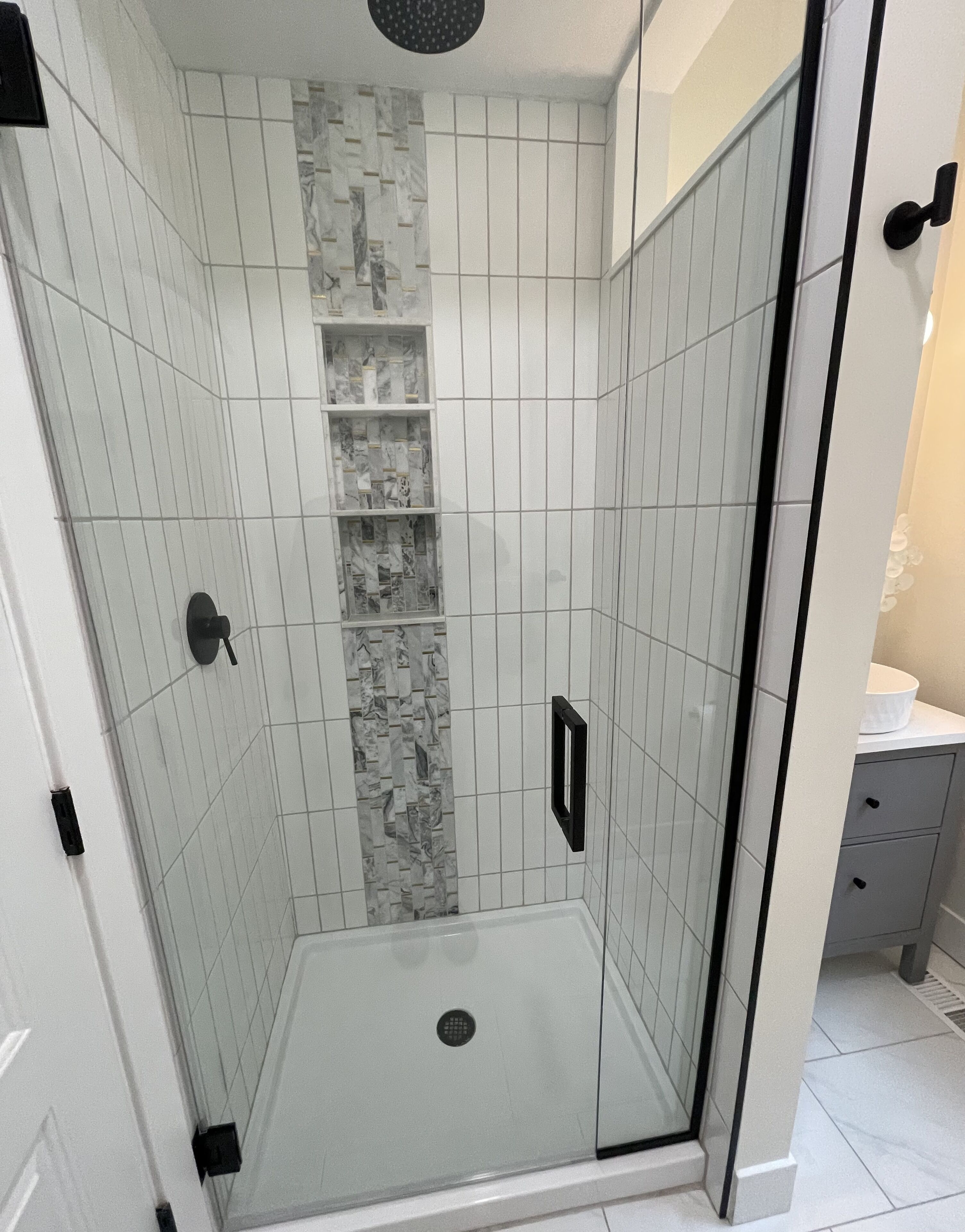 A walk-in shower with white tiles and a marble accent wall.