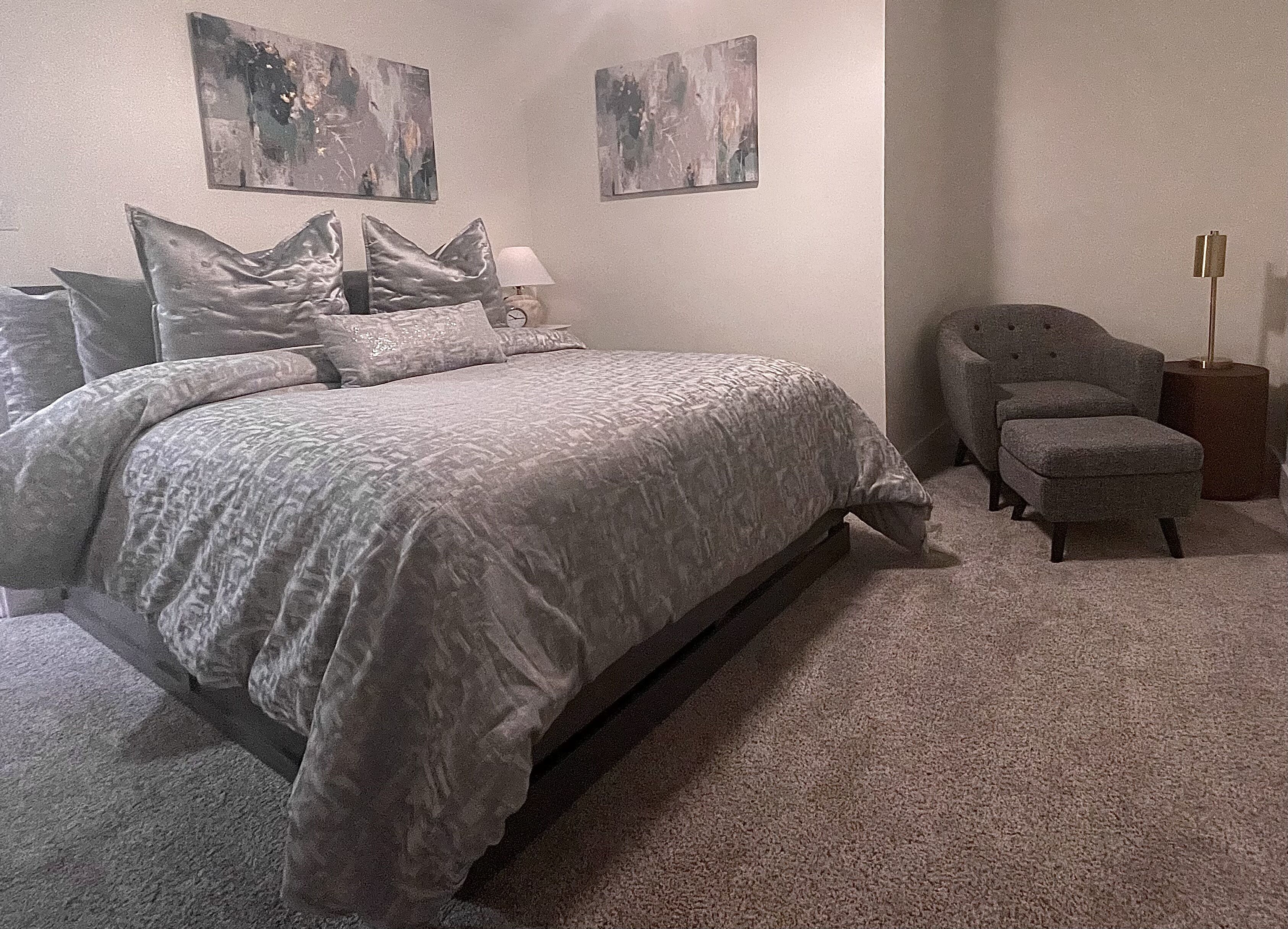 A bedroom with a bed, two pillows, a nightstand, a lamp, and a chair.