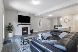 Una sala de estar moderna con chimenea, sofá de cuero, televisor de pantalla plana y un comedor con un reloj.