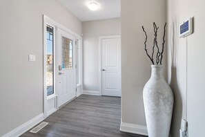 Un pasillo con una puerta blanca, un jarrón blanco con ramas y un termostato en la pared.