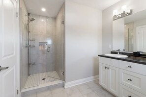 Un baño moderno con ducha envuelta en vidrio, tocador con lavamanos y un espejo grande.