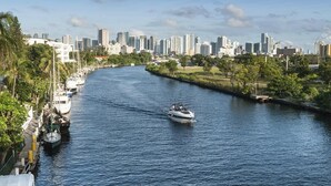 Ein Fluss mit Booten, im Hintergrund eine Stadtansicht und Uferbepflanzung.
