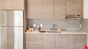 Eine moderne Küche mit hellen Holzschränken, einem Edelstahlkühlschrank, einer Spüle und einer gefliesten Spritzschutzwand.