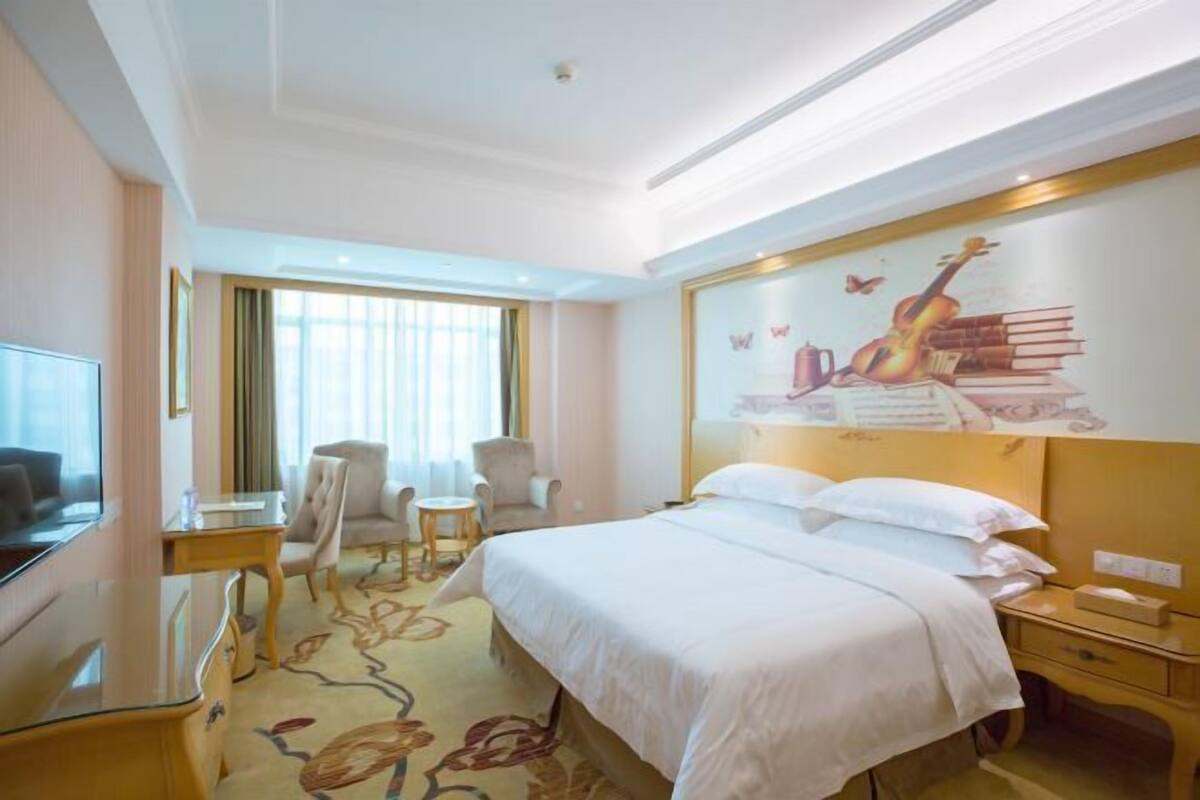 A hotel room with a bed, a desk, a chair, a television, and a mural on the wall.
