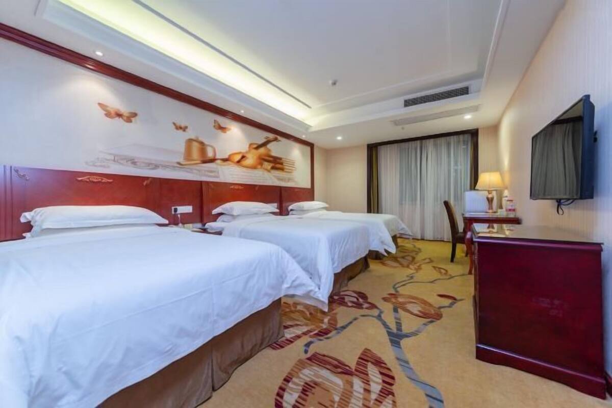 A hotel room with two beds, a large wall mural, a desk with a lamp, and a TV mounted on the wall.