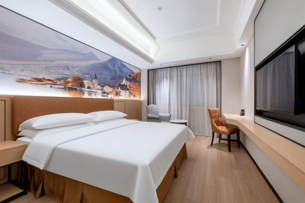 A hotel room with a large bed, a chair, a desk, and a TV.