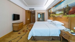 A hotel room with a large bed, a TV mounted on the wall, a wooden nightstand, and a painting on the wall. - Vienna Hotel Guangzhou Huadu Cultural Tourism City Shiling shop (Guangzhou)