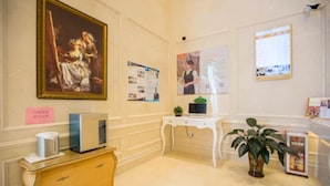 A room with a classic painting, a desk with a computer, a plant, and a small cabinet. - Vienna Hotel Guangzhou Huadu Cultural Tourism City Shiling shop (Guangzhou)