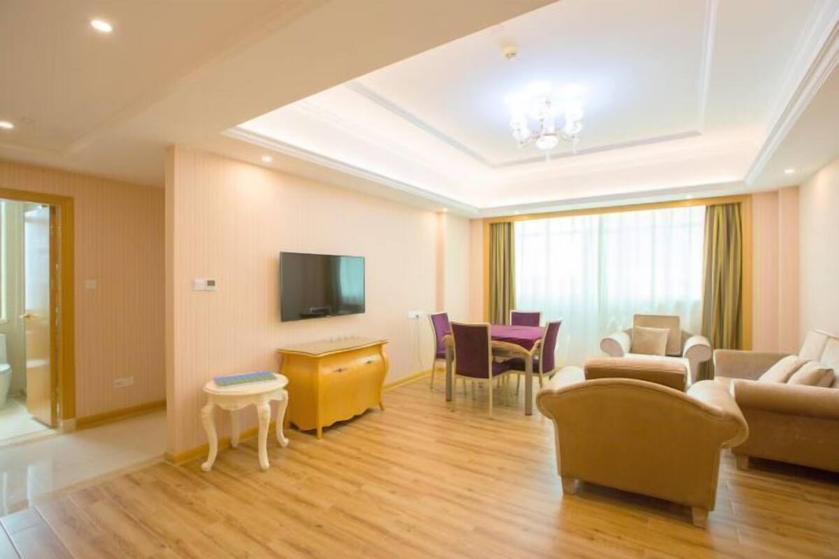 A modern living room with a flat-screen TV, a wooden cabinet, a dining table with chairs, and a sofa.