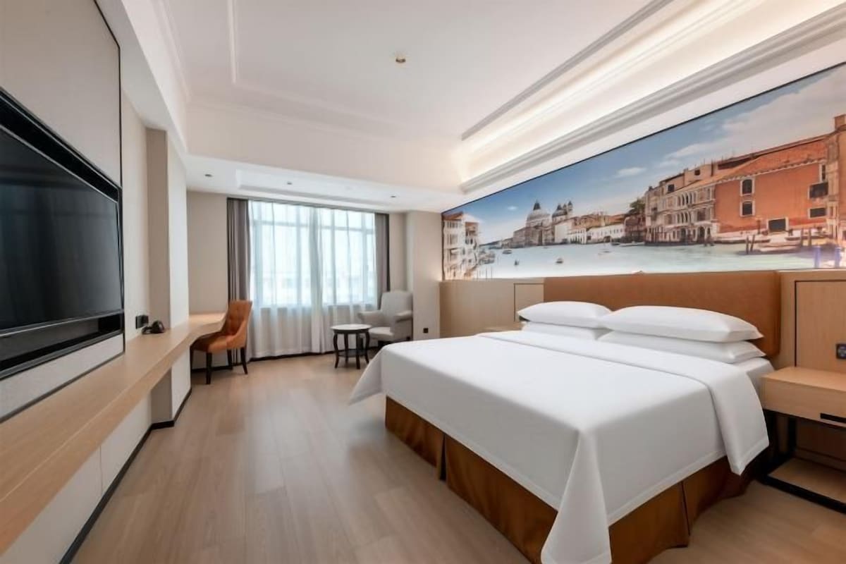 A hotel room with a bed, a TV, a desk, and a chair.