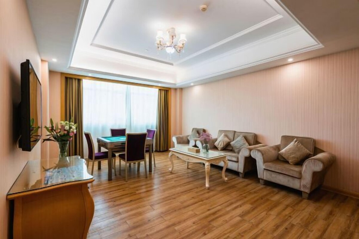 A hotel room with a dining area, sofa set, and a TV mounted on the wall.