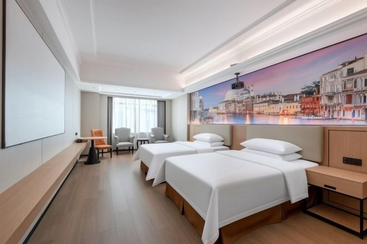 Une chambre d’hôtel avec deux lits, un bureau, une chaise et une grande fenêtre donnant sur le paysage urbain.