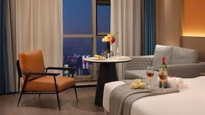 A hotel room with a bed, a chair, a small table with a vase of flowers, and a city view. - Dilunting International Hotel (Wansheng Yaocheng) (Chongqing)